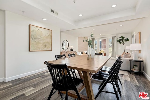 dining area with dark wood-type flooring, a raised ceiling, and french doors