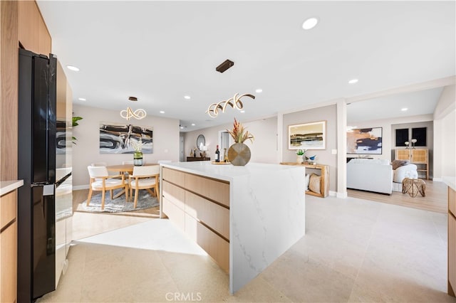 kitchen with oven, black refrigerator, a kitchen island, pendant lighting, and light stone countertops