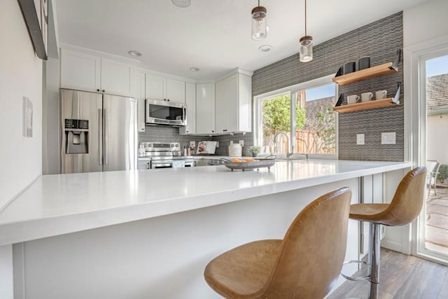 kitchen featuring appliances with stainless steel finishes, decorative light fixtures, white cabinets, a kitchen breakfast bar, and kitchen peninsula