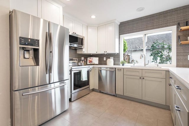 kitchen featuring white cabinetry, sink, decorative backsplash, light tile patterned floors, and stainless steel appliances