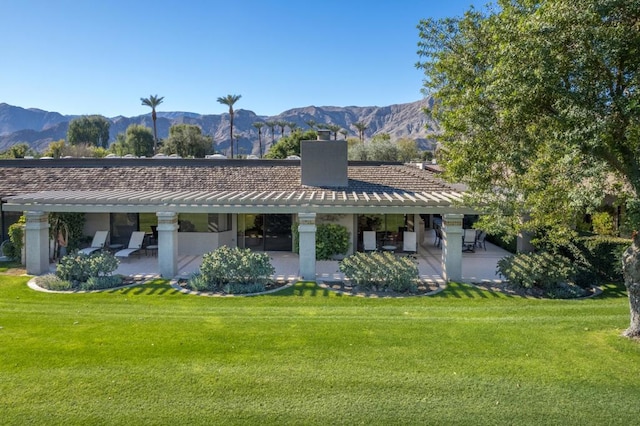 rear view of house with a patio, a mountain view, and a lawn