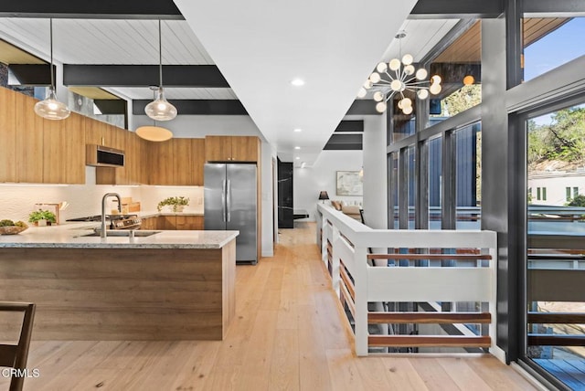 kitchen featuring light stone counters, decorative light fixtures, stainless steel fridge, light hardwood / wood-style floors, and backsplash