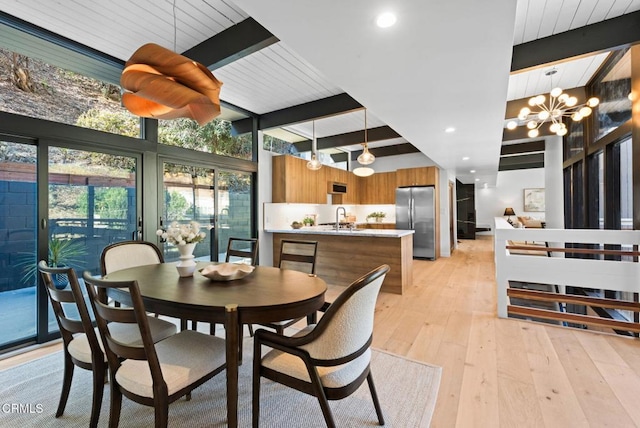 dining area with sink, a notable chandelier, beam ceiling, and light hardwood / wood-style flooring