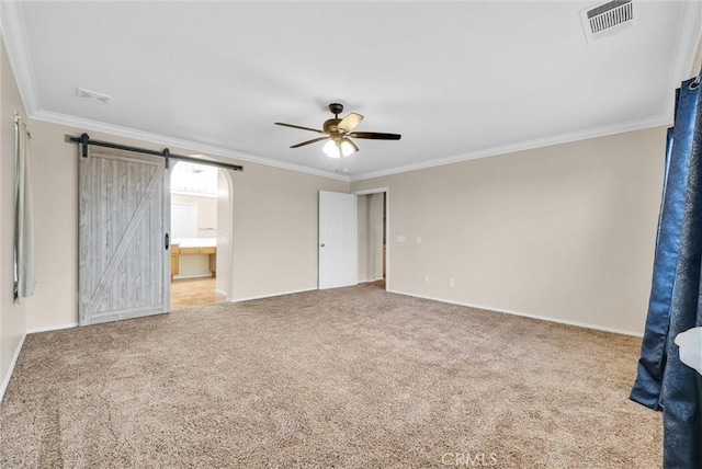 unfurnished bedroom featuring ensuite bath, ornamental molding, ceiling fan, a barn door, and carpet