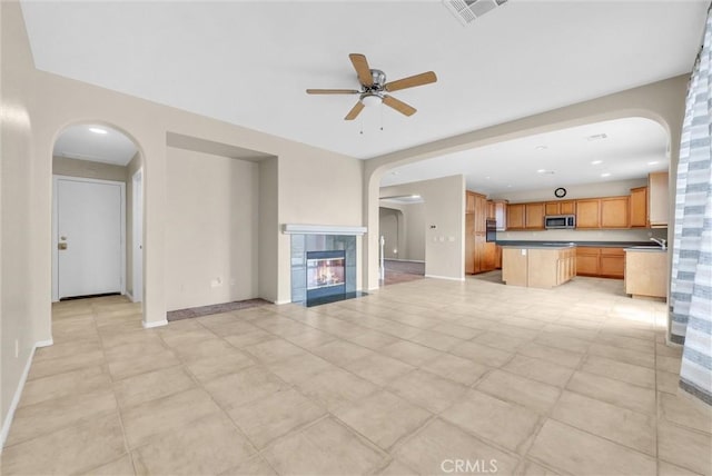 unfurnished living room with ceiling fan, a tiled fireplace, and sink