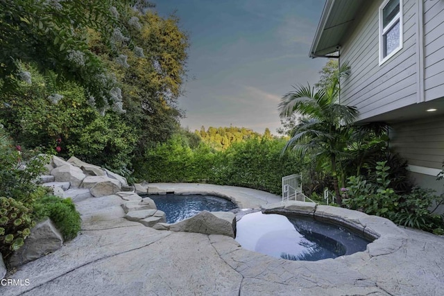 pool at dusk featuring an in ground hot tub