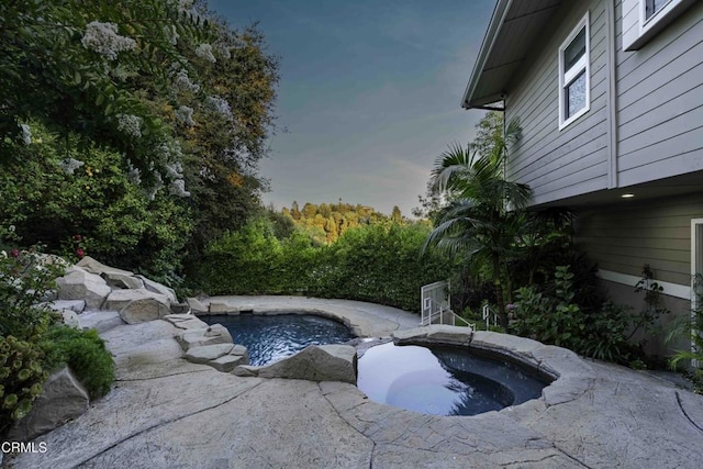 pool at dusk featuring an in ground hot tub