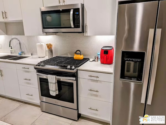 kitchen featuring sink, light tile patterned floors, appliances with stainless steel finishes, white cabinets, and backsplash