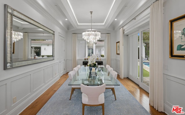 dining space featuring ornamental molding, a tray ceiling, a chandelier, and light wood-type flooring