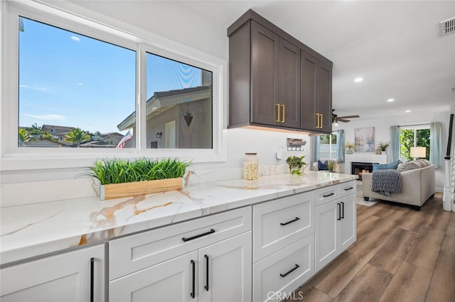 kitchen featuring dark wood-type flooring, dark brown cabinets, light stone countertops, and white cabinets