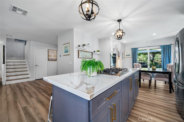 kitchen with appliances with stainless steel finishes, white cabinetry, hanging light fixtures, a center island, and a notable chandelier