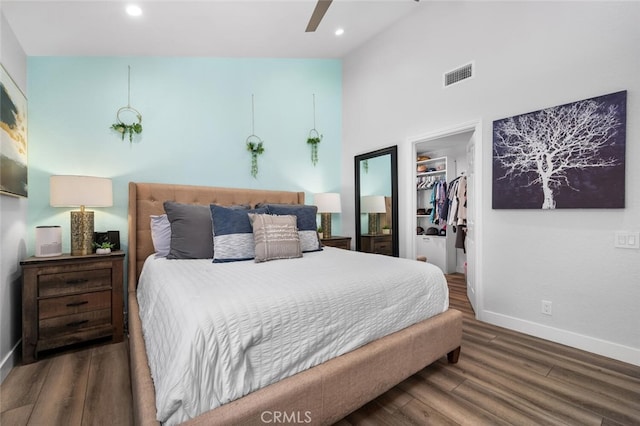 bedroom with a towering ceiling, a walk in closet, ceiling fan, dark wood-type flooring, and a closet