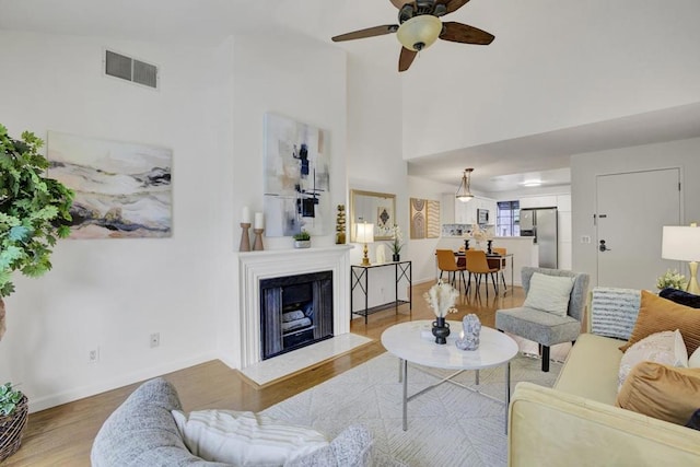 living room with ceiling fan, a towering ceiling, and light hardwood / wood-style flooring