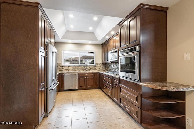 kitchen featuring light tile patterned flooring, dark brown cabinets, a raised ceiling, stainless steel appliances, and decorative backsplash