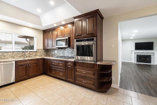 kitchen featuring sink, appliances with stainless steel finishes, dark brown cabinets, light stone countertops, and decorative backsplash