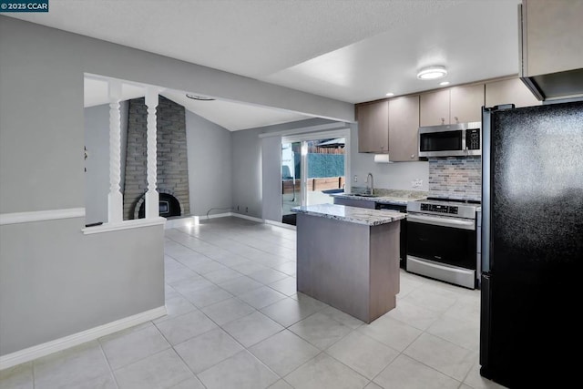 kitchen featuring appliances with stainless steel finishes, tasteful backsplash, lofted ceiling, light tile patterned floors, and light stone countertops