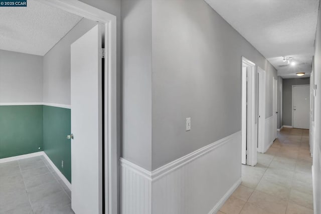 corridor with rail lighting, light tile patterned floors, and a textured ceiling