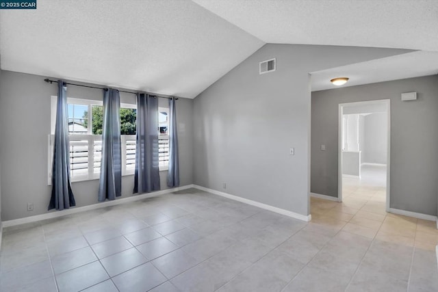 spare room featuring lofted ceiling, light tile patterned floors, and a textured ceiling