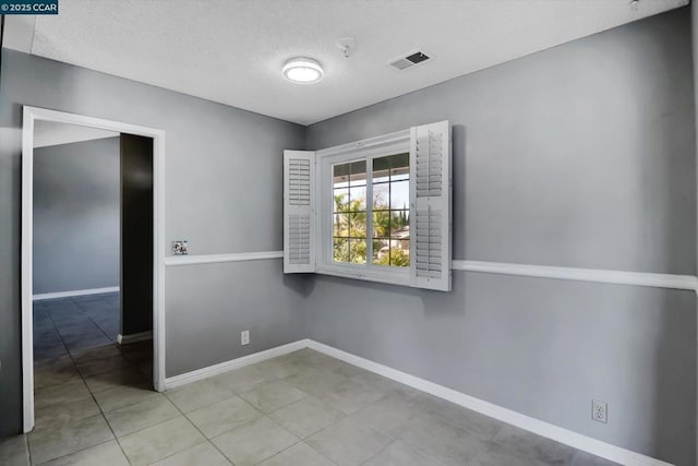 spare room with a textured ceiling and light tile patterned flooring