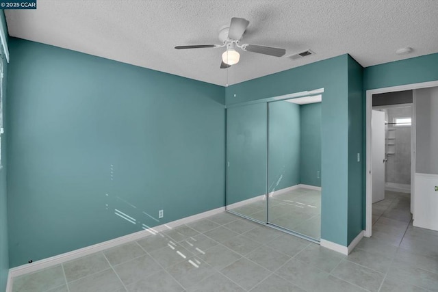 unfurnished bedroom with ceiling fan, light tile patterned flooring, a textured ceiling, and a closet