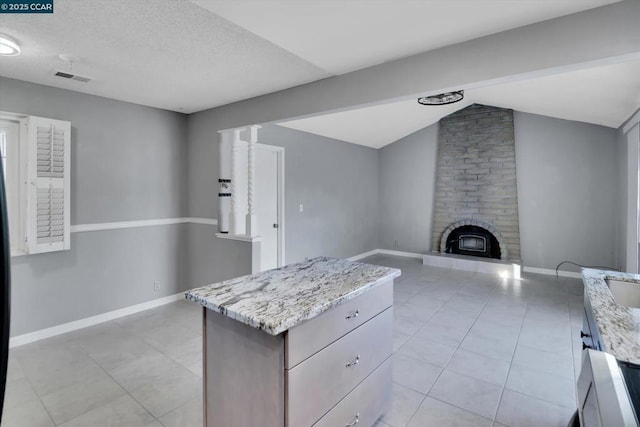 kitchen with vaulted ceiling, a fireplace, a center island, light tile patterned floors, and light stone countertops