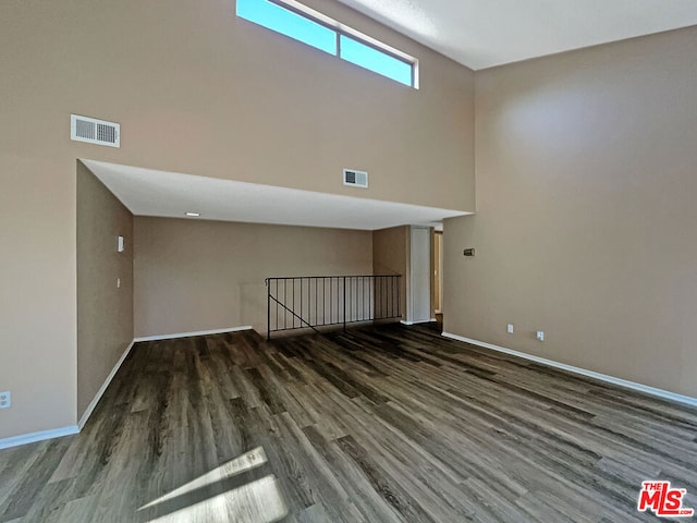 unfurnished living room with dark wood-type flooring and a towering ceiling