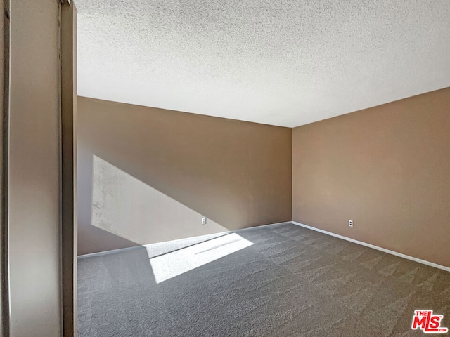 unfurnished room featuring a textured ceiling and dark colored carpet