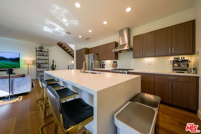 kitchen featuring wall chimney range hood, sink, dark wood-type flooring, refrigerator, and an island with sink