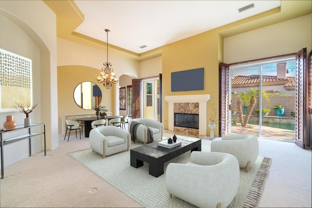 living room with a raised ceiling, a chandelier, light carpet, and a high end fireplace