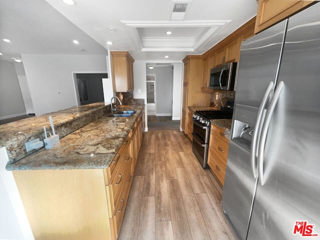 kitchen featuring sink, light wood-type flooring, appliances with stainless steel finishes, a raised ceiling, and dark stone counters