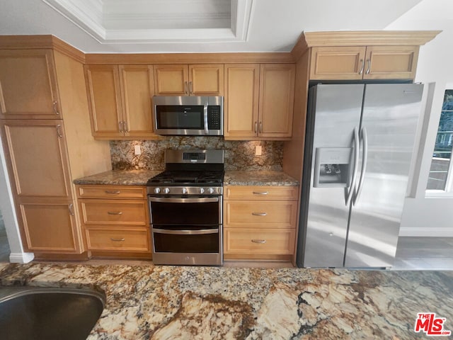 kitchen with dark stone counters, ornamental molding, a raised ceiling, stainless steel appliances, and decorative backsplash