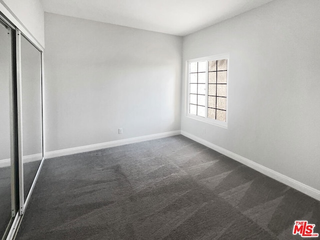 unfurnished bedroom with dark carpet and a closet