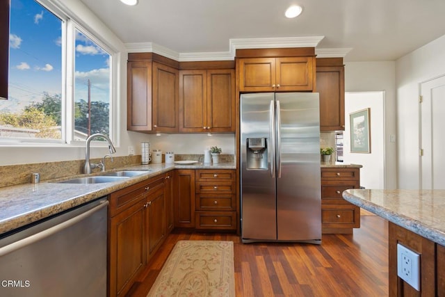 kitchen with sink, dark wood-type flooring, stainless steel appliances, light stone counters, and ornamental molding