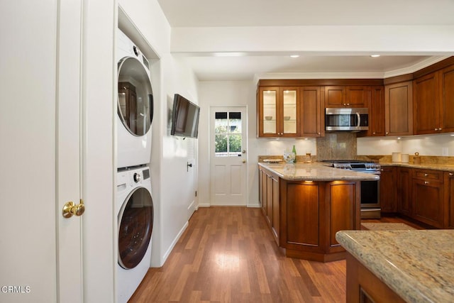 kitchen featuring stainless steel appliances, light stone counters, stacked washer / drying machine, decorative backsplash, and light wood-type flooring