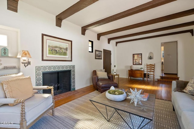 living room with beamed ceiling, wood-type flooring, and a tile fireplace