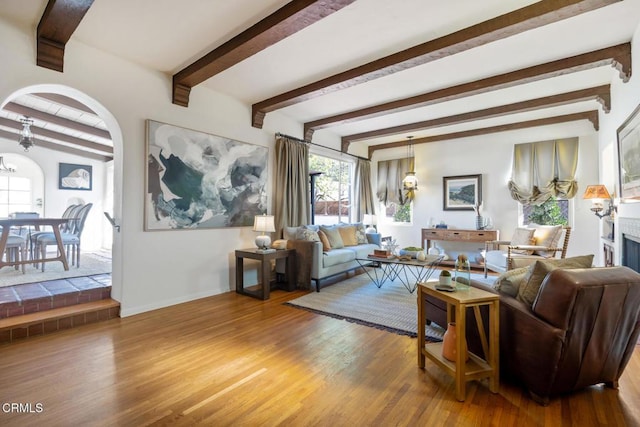 living room with wood-type flooring, an inviting chandelier, and beam ceiling