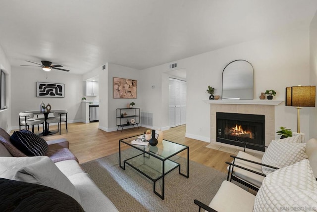 living room with a tile fireplace, ceiling fan, and light hardwood / wood-style flooring