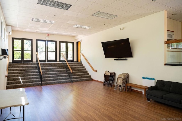 living room featuring an AC wall unit, wood-type flooring, and a drop ceiling