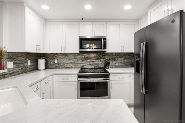 kitchen featuring appliances with stainless steel finishes, sink, white cabinets, decorative backsplash, and light stone countertops