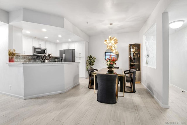 kitchen featuring decorative light fixtures, appliances with stainless steel finishes, kitchen peninsula, white cabinets, and backsplash