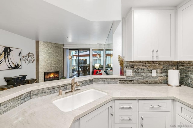 kitchen featuring a fireplace, white cabinetry, sink, decorative backsplash, and kitchen peninsula