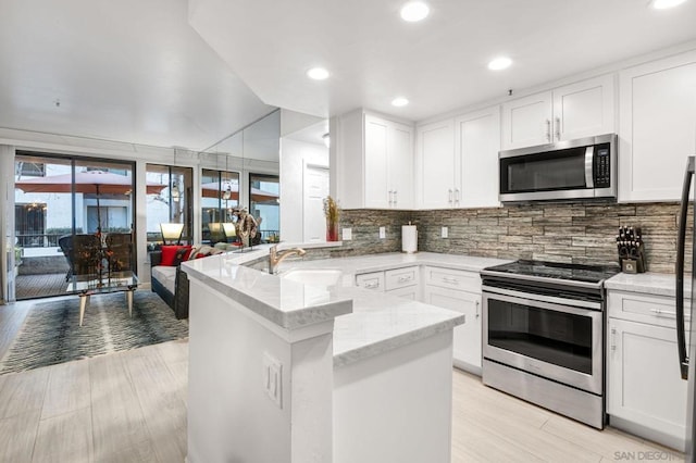 kitchen featuring appliances with stainless steel finishes, tasteful backsplash, white cabinetry, sink, and kitchen peninsula