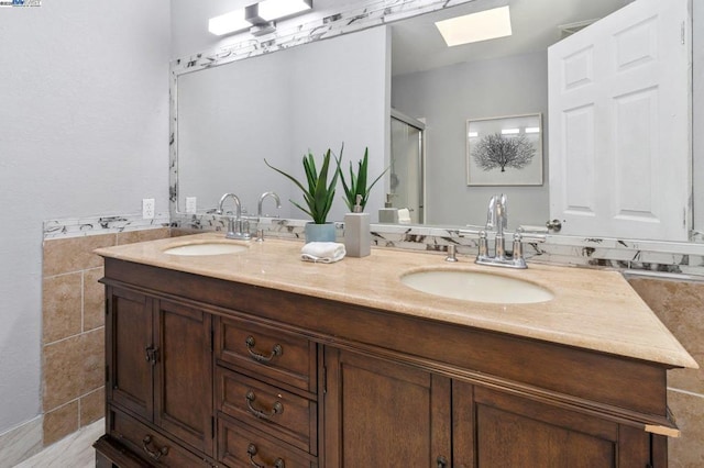 bathroom with tile walls, vanity, a skylight, and a shower with shower door