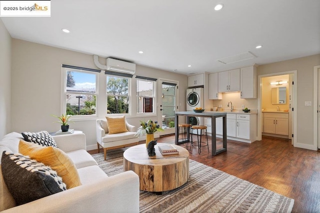 living room with stacked washer and clothes dryer, sink, a wall mounted AC, and dark hardwood / wood-style flooring