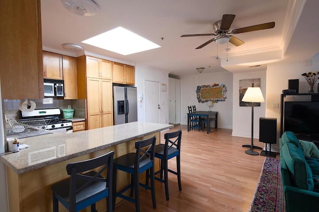 kitchen featuring a breakfast bar area, light stone counters, a skylight, light wood-type flooring, and appliances with stainless steel finishes