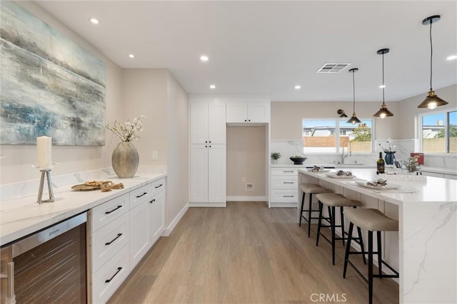 kitchen featuring white cabinetry, decorative light fixtures, light stone countertops, and wine cooler