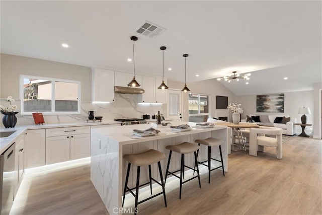 kitchen featuring white cabinetry, a center island, light stone counters, a kitchen bar, and decorative light fixtures