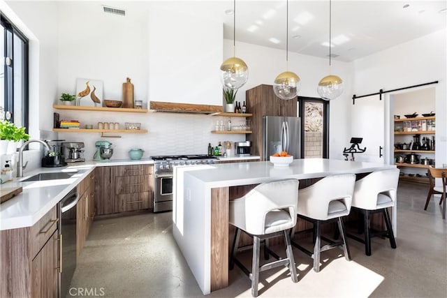 kitchen with a kitchen bar, sink, hanging light fixtures, appliances with stainless steel finishes, and a barn door