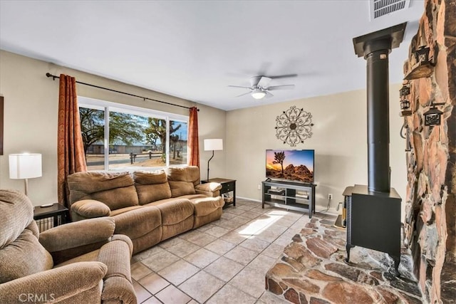 living room with light tile patterned flooring, ceiling fan, and a wood stove