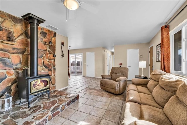 living room featuring ceiling fan, light tile patterned floors, and a wood stove